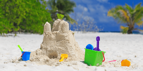 Sand castle with sand toys next to it. 